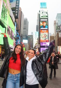 two women standing in the middle of a busy city street, one holding her arms up