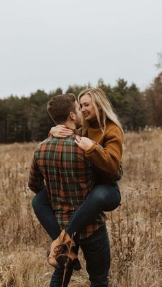 a man and woman are hugging in the middle of a field with tall brown grass