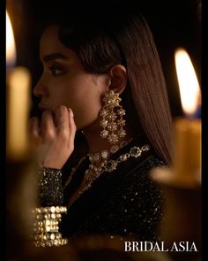 a woman with long hair wearing gold jewelry and holding her hand up to her face