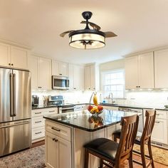 a kitchen with white cabinets and an island in the middle is lit by a ceiling fan