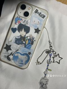 an iphone case with charms attached to it on top of a white cloth covered table