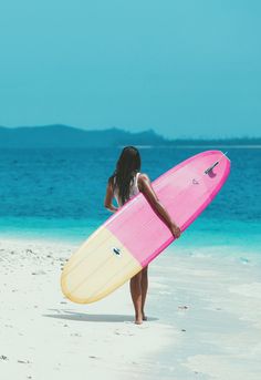 a woman holding a surfboard on top of a sandy beach next to the ocean