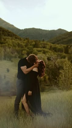 a man and woman embracing in the middle of a field with mountains in the background