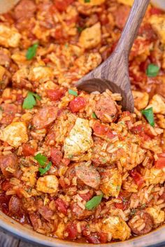 a wooden spoon in a large pot filled with rice and sausages, garnished with parsley