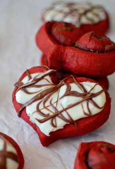 three red heart shaped pastries with chocolate drizzled on top and white frosting