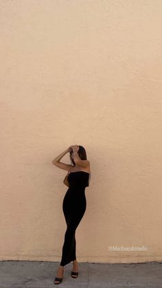 a woman leaning against a wall with her hands on her head and wearing high heels