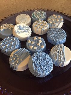 nine decorated cookies sitting on top of a black plate in front of a brown wall