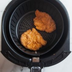 two fried chicken patties in a black air fryer on a white counter top