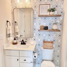 a white toilet sitting under a bathroom mirror next to a wall mounted shelf filled with towels