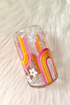 a clear glass with flowers and rainbows painted on the inside is sitting on a white fur surface