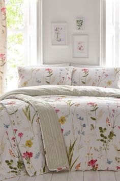 a white bed with flowers on it in front of a window and pictures above the bed