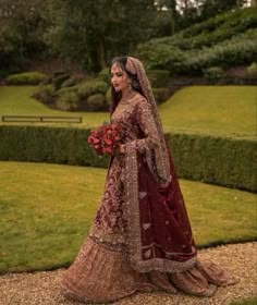 a woman in a red and gold bridal gown holding a bouquet of flowers on her wedding day