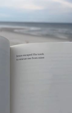 an open book sitting on top of a beach next to the ocean with words written in it