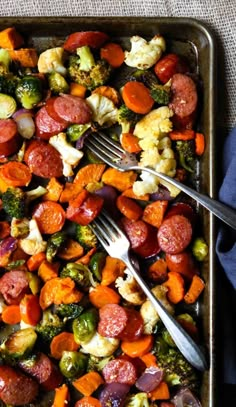 a tray filled with sausage, broccoli and cauliflower next to a fork