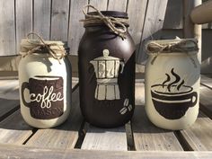 three painted mason jars sitting on top of a wooden table next to each other with coffee cups drawn on them