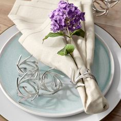 the napkins are wrapped in silver wire and have purple flowers on top of them