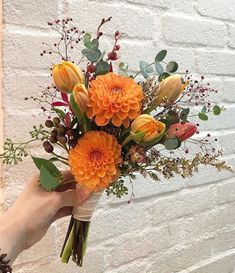 a person holding a bouquet of flowers in front of a brick wall