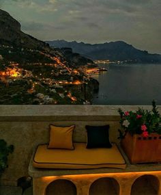 an outdoor seating area with potted plants and lights on the water's edge