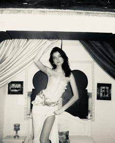 black and white photograph of a woman posing in front of a bed with drapes