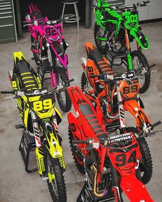 several dirt bikes are lined up in a row on the floor, with numbers painted on them