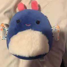 a blue and white stuffed animal with ears on it's head sitting on top of a bed