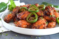 a white plate topped with chicken covered in sauce and jalapenos next to green peppers