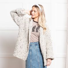 a woman standing in front of a white wall wearing a denim skirt and a sweater