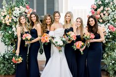 a group of women standing next to each other in front of an arch with flowers