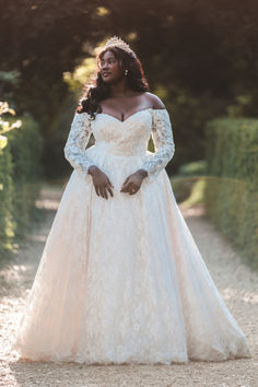 a woman in a white wedding dress standing on a dirt road wearing a tiara