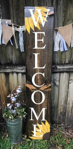 a wooden welcome sign sitting next to a potted plant on the side of a fence