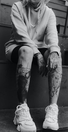 black and white photograph of a woman with tattoos on her legs sitting on a bench