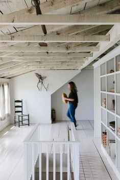 a woman standing in an empty room with white walls and wooden beams on the ceiling