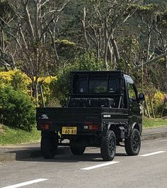 a black truck is driving down the road near some trees and bushes on both sides