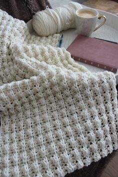 a crocheted blanket sitting on top of a table next to a cup of coffee