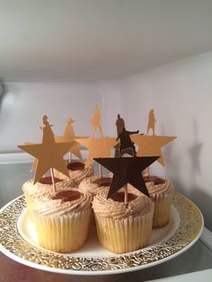 cupcakes on a plate with gold stars and people in the sky toppers