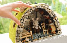 a hand is reaching into a miniature house made out of rocks and stones with a rabbit inside