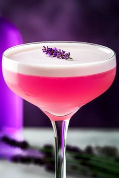 a pink drink with lavender sprigs on the rim in front of a purple background