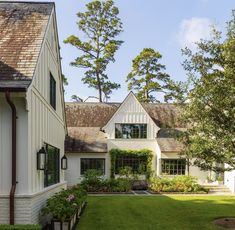 a white house with lots of windows and plants in the front yard, surrounded by trees