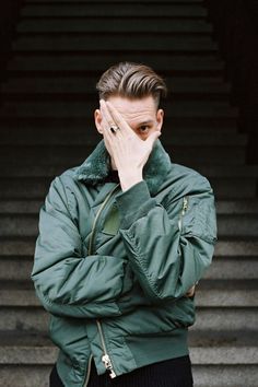 a man in a green jacket covers his face with his hands while standing on some steps