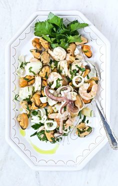 a white plate topped with shrimp, onions and green garnish next to a fork