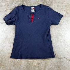 "Vintage Y2K navy blue shirt. Ribbed, three button front, and cropped cut. Good condition, minor wear. Brand: Tommy Jeans Size: Women's Large Measurements: 21\" long 18\" pit to pit" Blue Short Sleeve T-shirt With Buttons, Navy Short Sleeve Tops With Button Closure, Blue Short Sleeve Tops With Snap Buttons, Blue Short Sleeve Top With Snap Buttons, Blue T-shirt With Button Closure And Crew Neck, Casual Blue T-shirt With Buttons, Fitted Blue Tops With Snap Buttons, Blue Crew Neck T-shirt With Buttons, Navy Button-up Top With Buttons