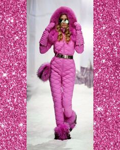 a woman in pink is walking down the runway wearing a fur hat and purple jumpsuit