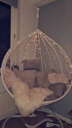 a white hanging chair with pillows and lights on the ceiling in a room next to a window