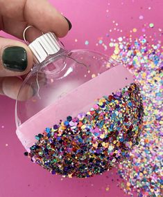 a hand holding a bottle filled with confetti and sprinkles on a pink background