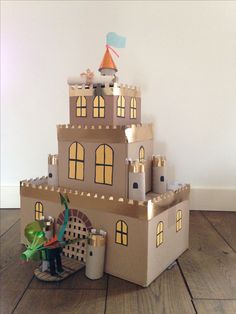 a castle made out of cardboard sitting on top of a wooden floor next to a potted plant