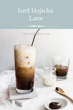 iced hojcha latte in a tall glass on a white table with two spoons next to it