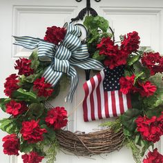 a wreath with red flowers and an american flag on it hanging from the front door