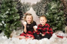 two children are sitting in the snow with christmas trees behind them and one child is holding an egg