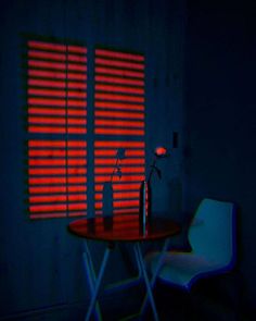 a room with a table, chair and window covered in red light from the blinds