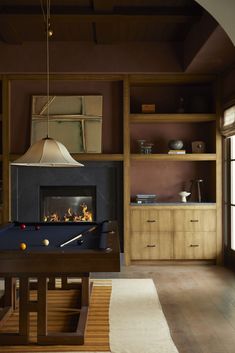 a billiard table in front of a fireplace with a lamp on it and shelves behind it